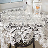 White lace tablecloth with embroidered rose design set on a dark wooden table.