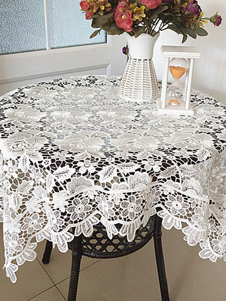 White lace tablecloth with embroidered rose design set on a dark wooden table.