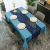 A long table set for a meal with blue tablecloth, white plates, and silverware in a modern interior.