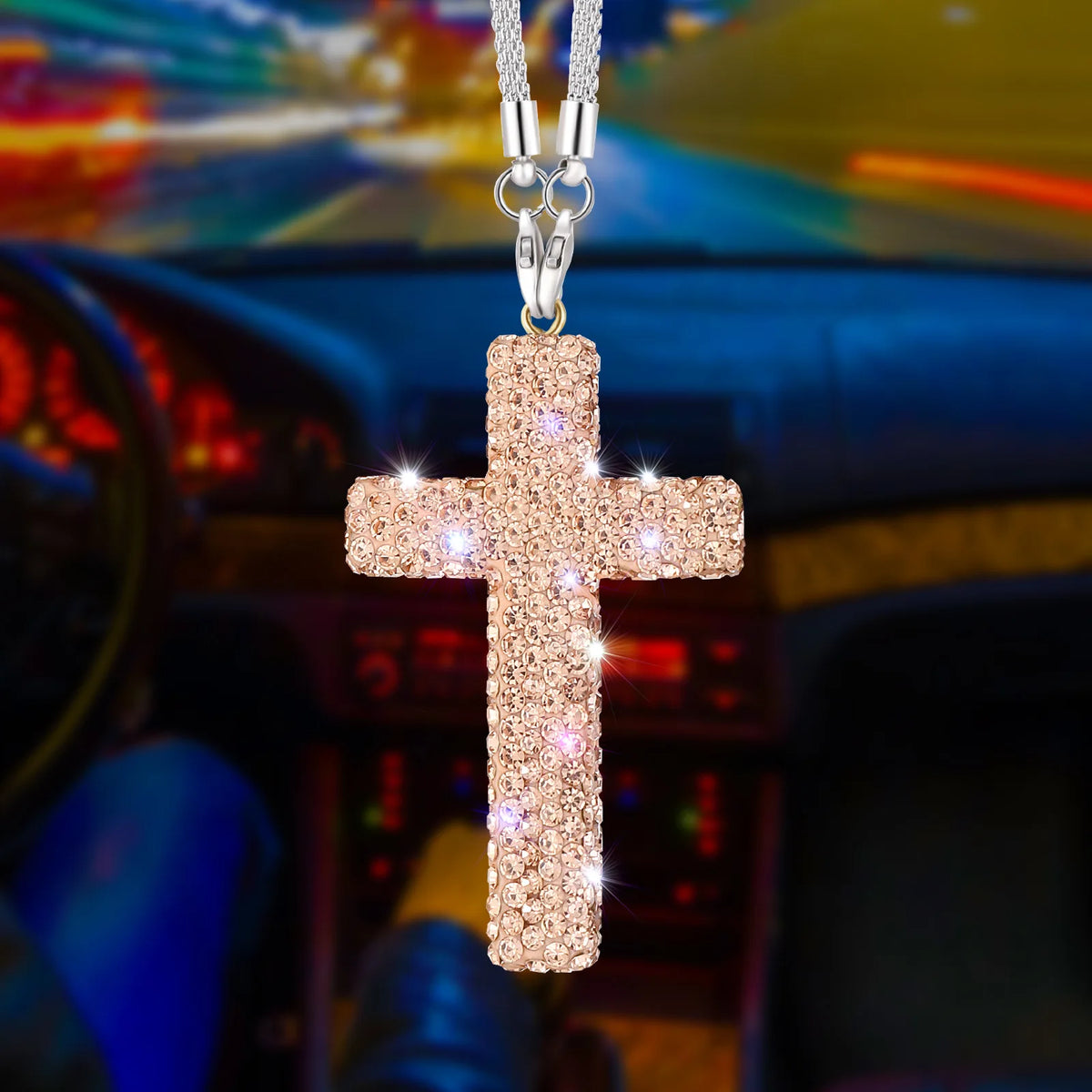 A stainless steel rhinestone cross pendant hanging from a chain, set against a blurred car interior background.