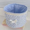 Cesta de almacenamiento con forma de corazón, acolchada a cuadros azul claro y blanco, con ribete de encaje y un lazo blanco.