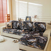 A dark floral patterned elastic sofa cover protecting a light-colored sofa in a bright room.