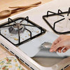 A hand places a reusable gas stove burner protector onto a stovetop grate.