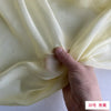 A hand is folding a piece of pale yellow silk chiffon fabric.