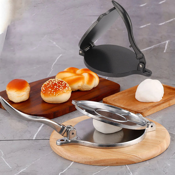 Manuelle Aluminium-Tortillendrücke mit gebackenen Brötchen und einem weißen Teigball auf Holz