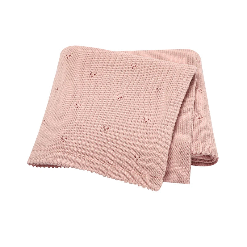 A folded light pink knitted cotton baby blanket with small eyelet details.