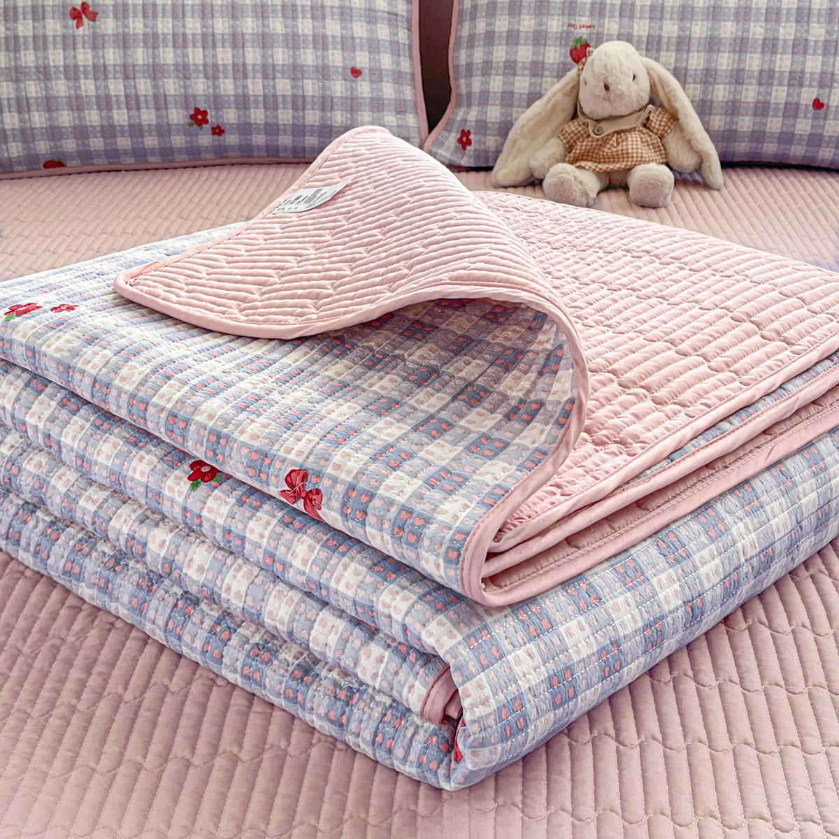 Pink quilted blanket folded next to a stuffed elephant on a pink bed.