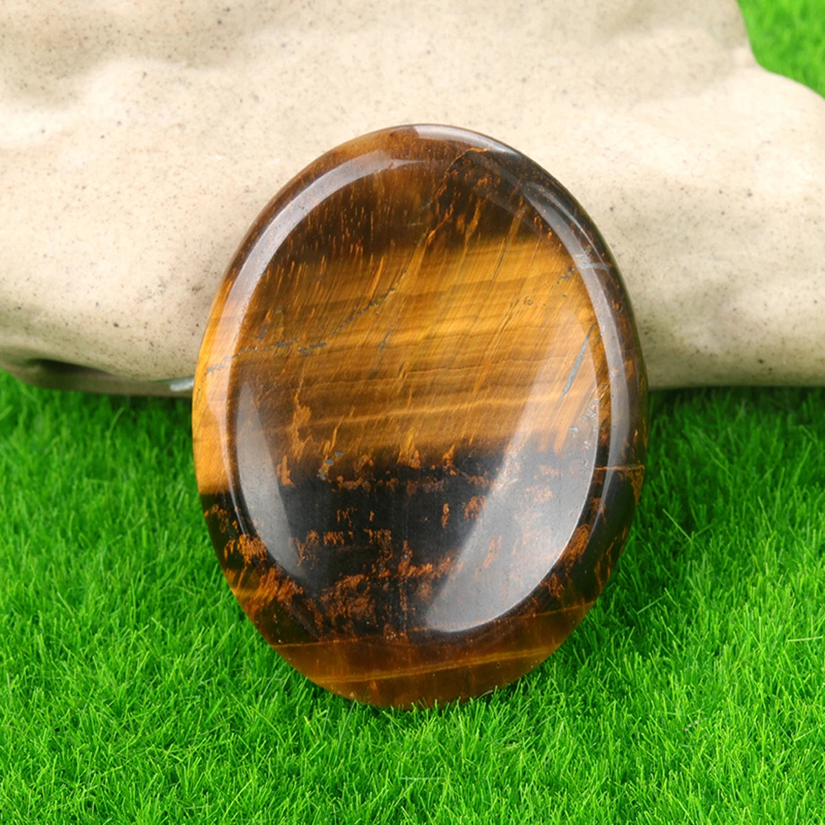 A polished, oval amber-colored natural crystal stone resting on green grass.