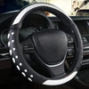 A close-up view of a black steering wheel with a heart-shaped white patterned cover inside a car interior.