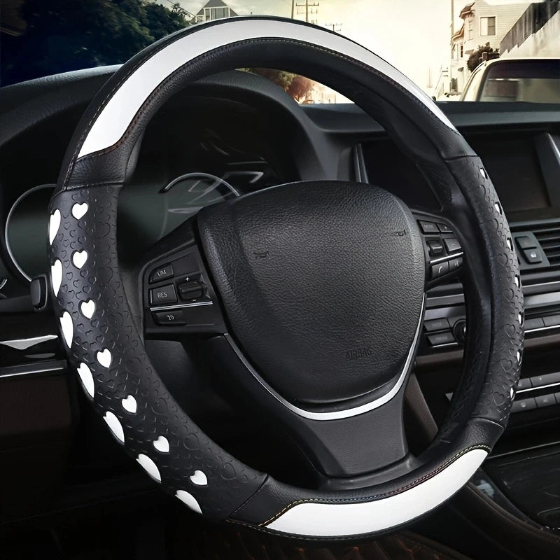 A close-up view of a black steering wheel with a heart-shaped white patterned cover inside a car interior.