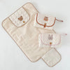 A beige foldable portable diaper changing pad with padded sections featuring cute animal designs.
