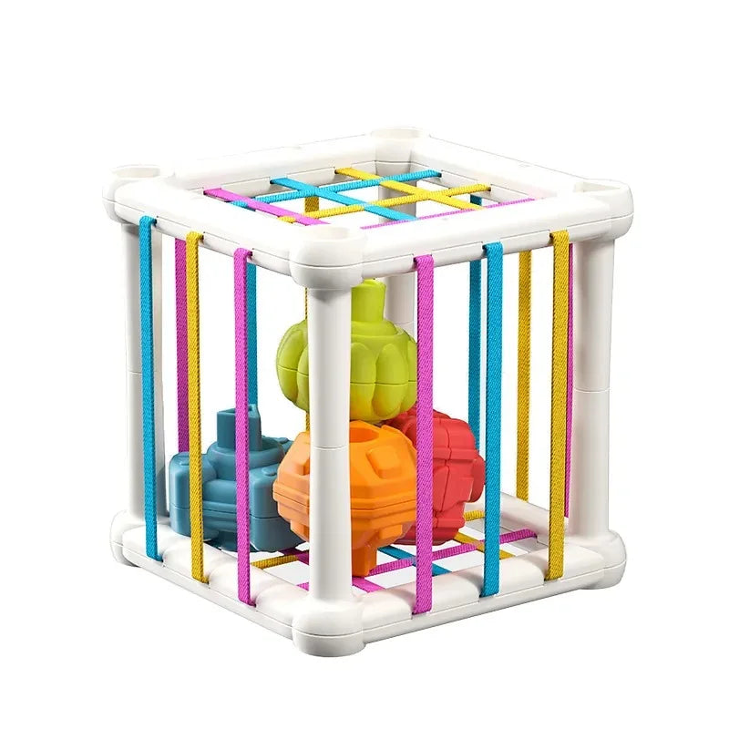 A white cube sorter toy with colorful elastic bands and various shapes for Montessori learning.