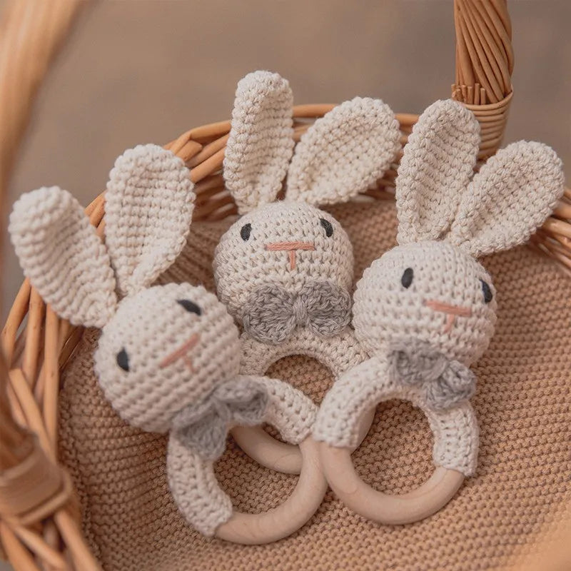 A handmade crochet bunny rattle featuring natural wood teether rings, set in a woven basket.