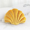 A golden velvet shell print throw pillow resting on white bedding.