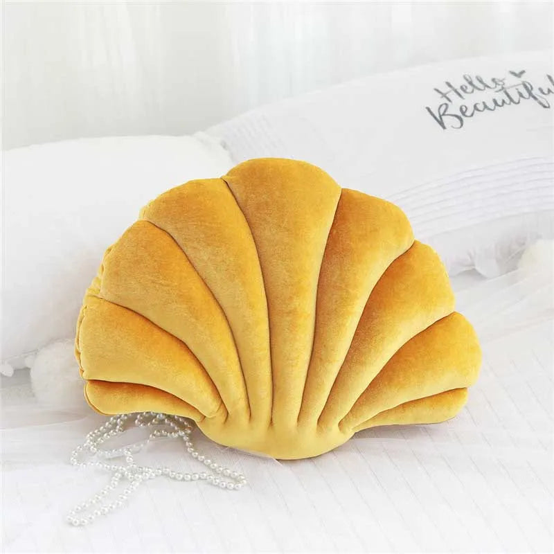 A golden velvet shell print throw pillow resting on white bedding.