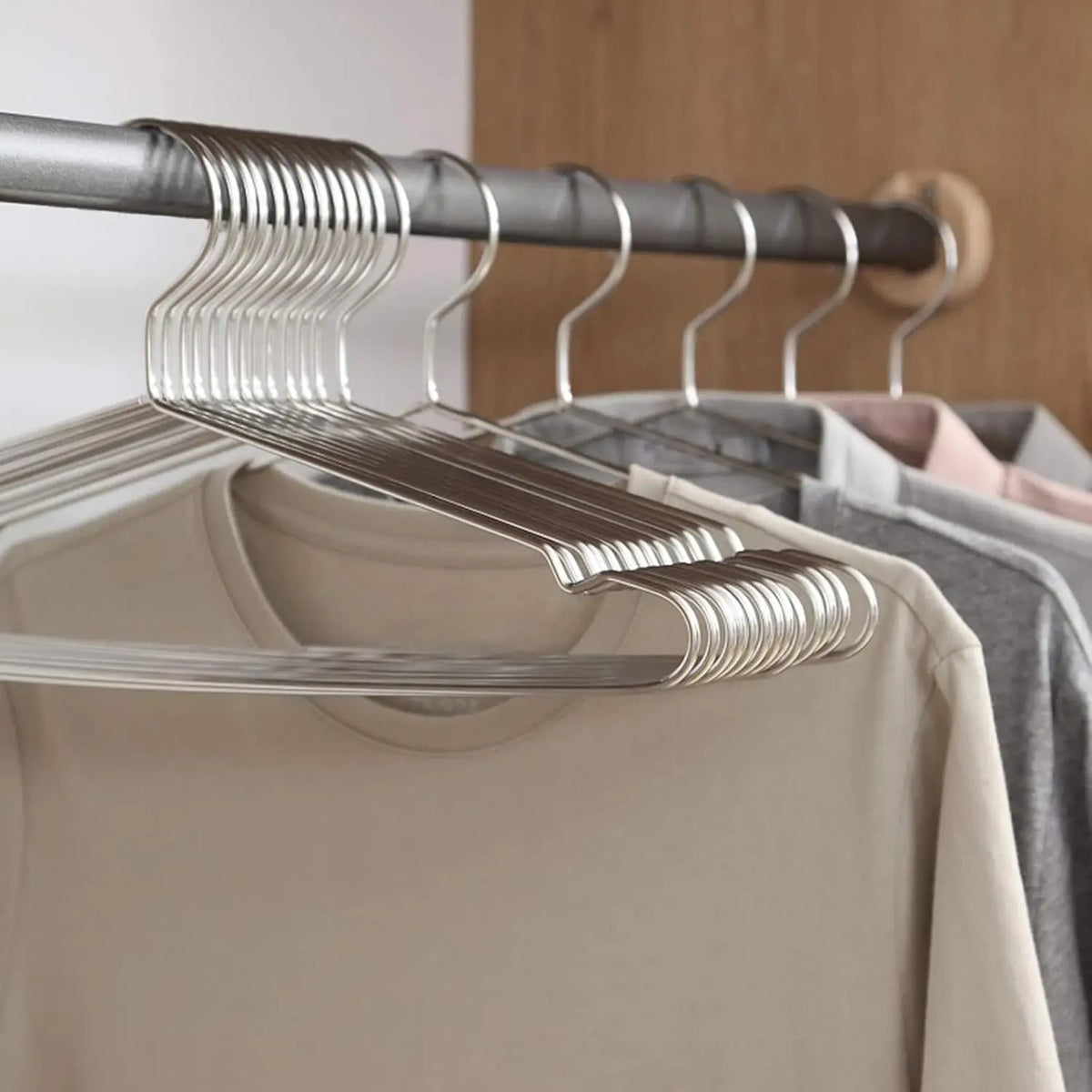 A close-up view of heavy-duty stainless steel wire clothes hangers hanging on a wooden rod.