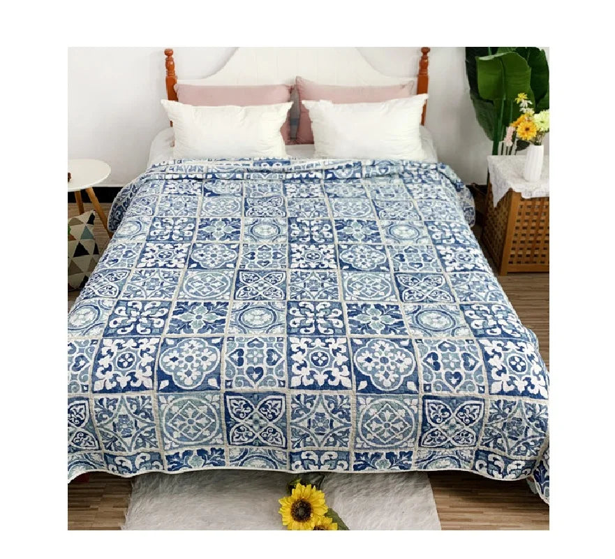 A blue and white patchwork cotton bedspread displayed on a bed with white pillows.