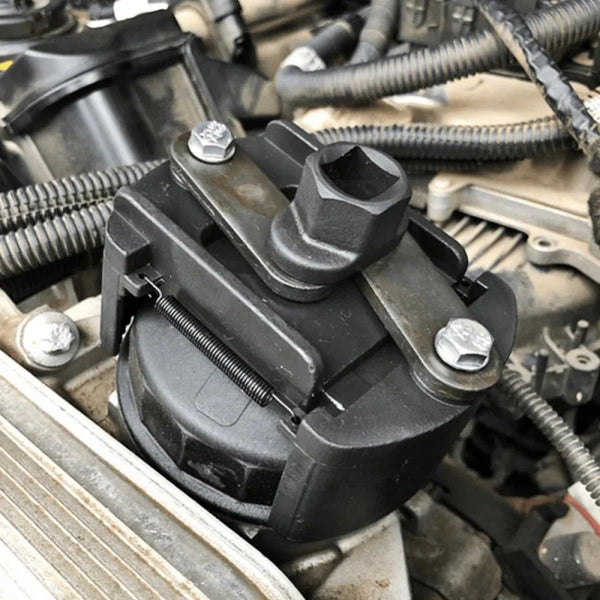 A black adjustable oil filter wrench is shown gripping an oil filter on a vehicle engine component.