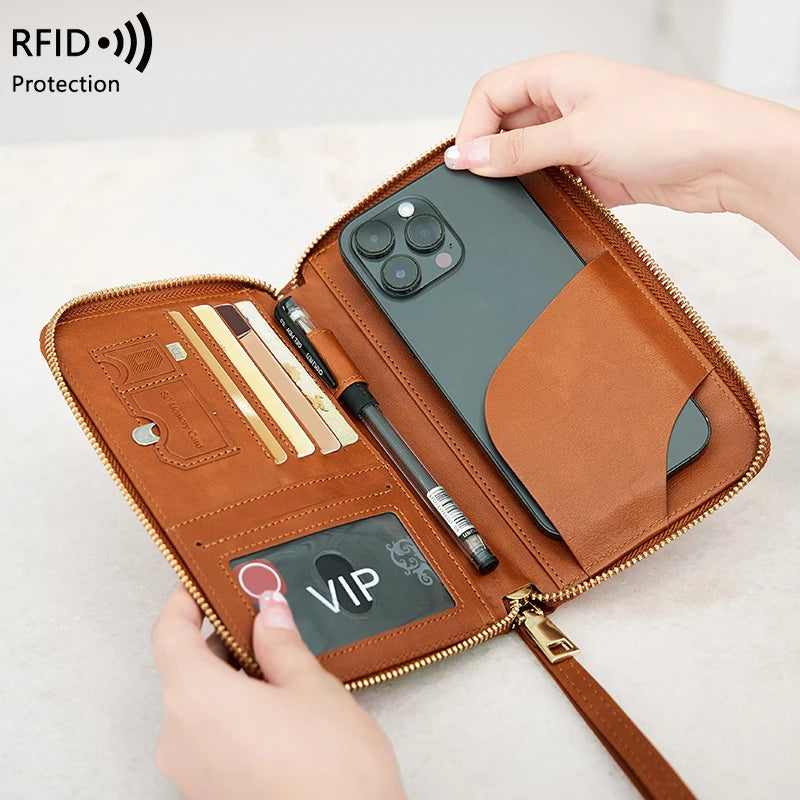 A brown leather RFID-blocking travel wallet is shown open, displaying a smartphone and various accessories.