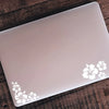 A white laptop is shown with a floral decal sticker design on the lid, placed on a dark wooden surface.