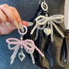 A close-up of a pearl bow keychain with a heart charm attached to a black leather bag.