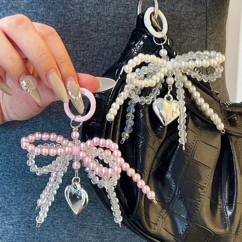 A close-up of a pearl bow keychain with a heart charm attached to a black leather bag.