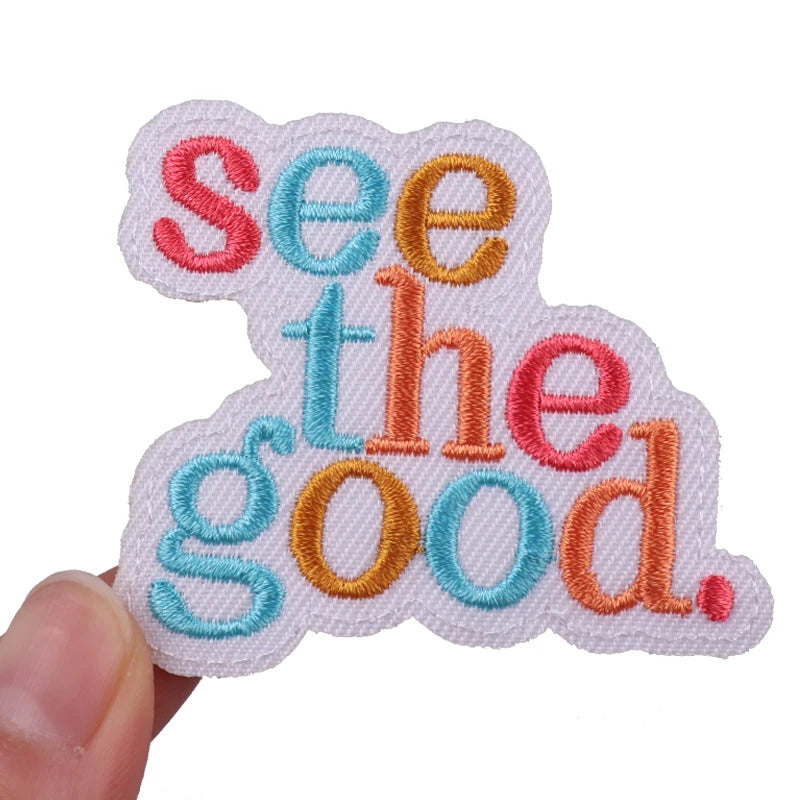 A set of pink and orange embroidered iron-on patches spelling out the words See the good.