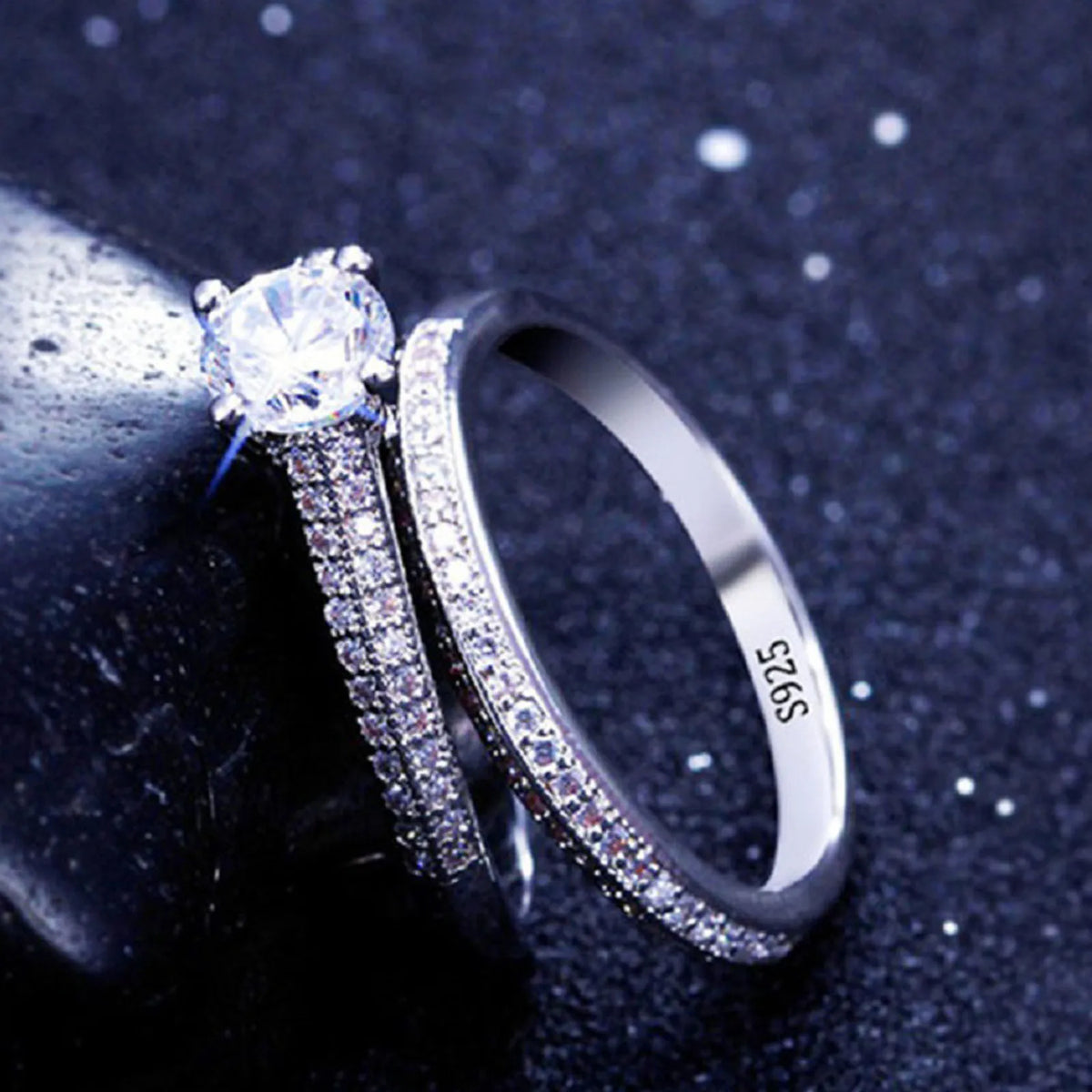 A close-up of a sterling silver ring set featuring a halo-set diamond ring and a pave zircon band on a dark surface.