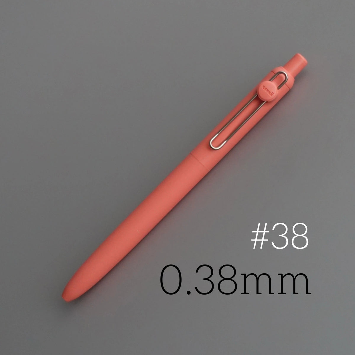 A close-up view of a pink Uni ZENTO Quick-Dry Gel Pen with a silver clip, shown diagonally on a gray surface.