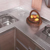 A kitchen countertop with a stainless steel sink, wooden bowl of fruit, and a stovetop area.
