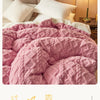 A close-up of a pink textured velvet duvet cover and blanket displayed on a bed.