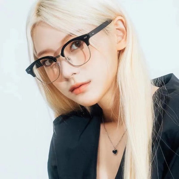 A close-up portrait of a woman wearing black retro half-frame blue light blocking glasses and a dark blazer.