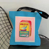 A blue canvas tote bag with a rectangular print featuring the text SARDINAS ORTIZ and an illustration of a fish.