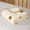 A stack of white cotton gauze baby swaddle blankets with bear print designs resting on a white bed.