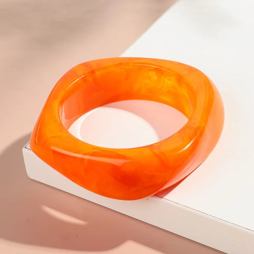 Bracelet manchette acrylique orange et translucide sur une boîte blanche.
