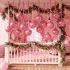 A pink nursery decorated with fairy lights and pink balloons, featuring a white crib and pink bedding.
