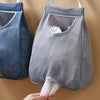 A gray mesh garbage bag holder is shown hanging on a wall, with a hand holding the bottom opening.