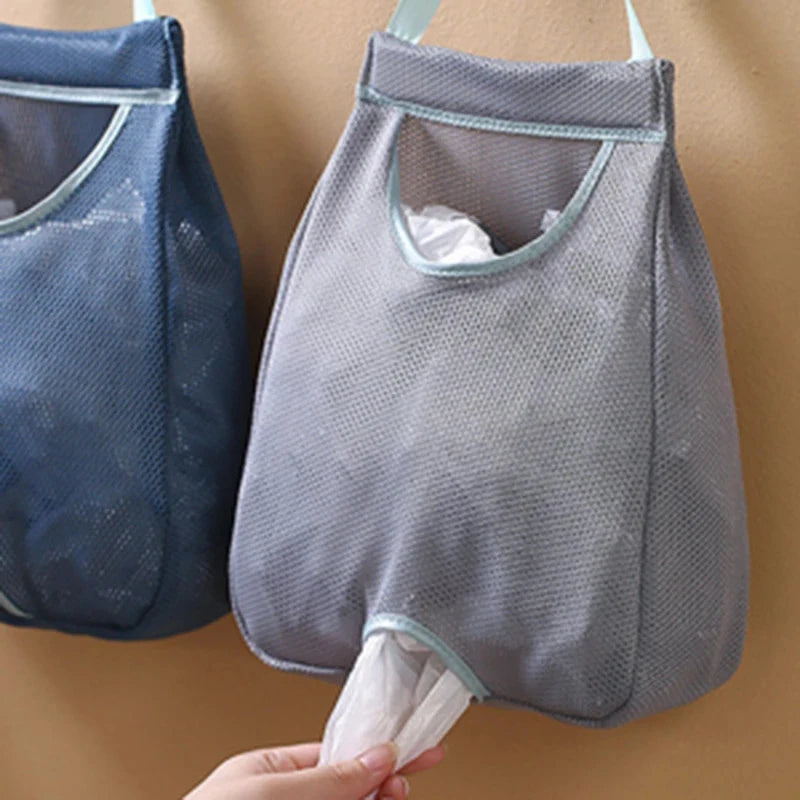 A gray mesh garbage bag holder is shown hanging on a wall, with a hand holding the bottom opening.