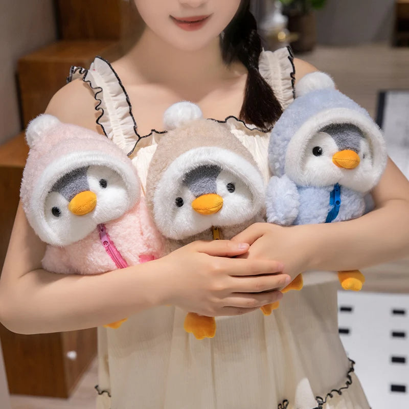 A woman holds two adorable penguin plush toys with fluffy white and blue hats.