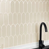 A kitchen backsplash featuring white arched tiles on a beige wall above a black countertop and faucet.