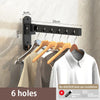 Black foldable wall-mounted clothes drying rack with six holes installed on a beige wall.