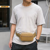 A person wearing a light gray t-shirt and dark pants, featuring a tan tactical MOLLE waist pack.