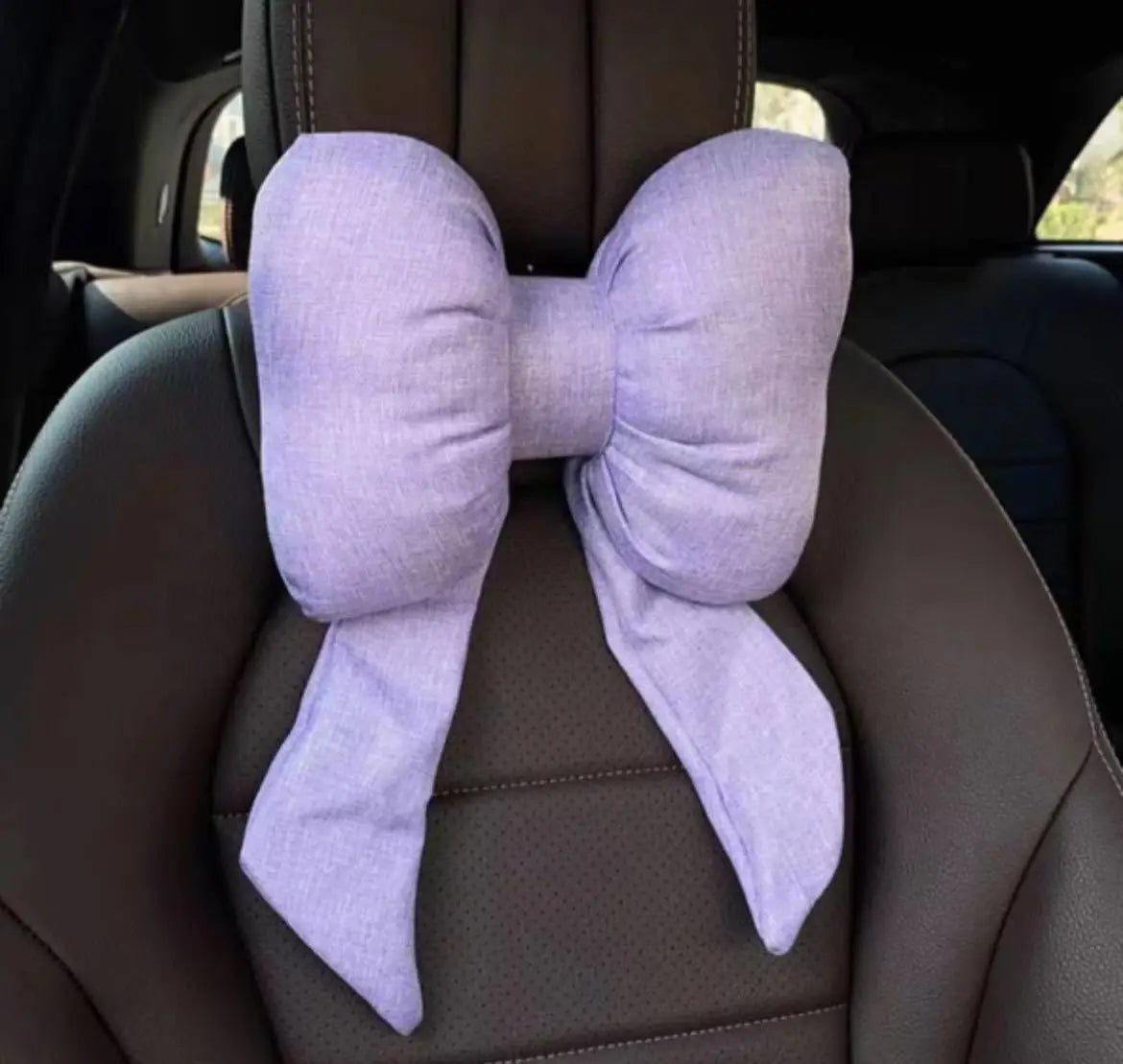 A lavender butterfly bow tie neck pillow with a textured cotton and linen cover is shown in a car seat interior.