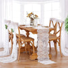 A wooden dining table set for a meal with embroidered floral lace table runners and sheer white fabric on a bright windowsill