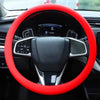 A red silicone steering wheel cover is shown inside a car, featuring a black steering wheel and controls.