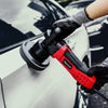 A hand wearing a glove is using a red electric polisher with a black pad on a white car surface.