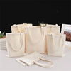 Several natural canvas shopping tote bags in beige and off-white colors are displayed on a white surface.