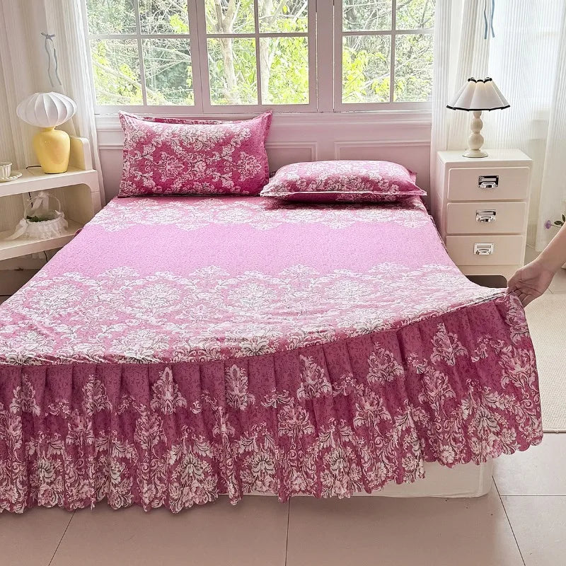 A pink floral print bed skirt and pillowcase set displayed on a bed in a bright room.