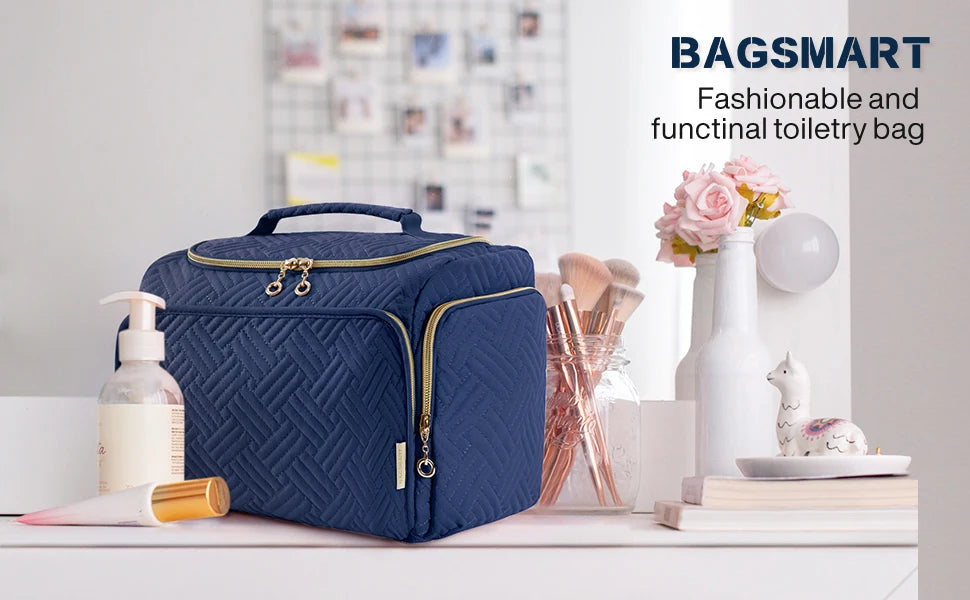 A navy blue bagsmart toiletry bag with a handle sits on a white surface next to various grooming tools and flowers.
