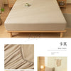 A beige fitted bed sheet set and pillow displayed on a wooden bed frame with natural light.